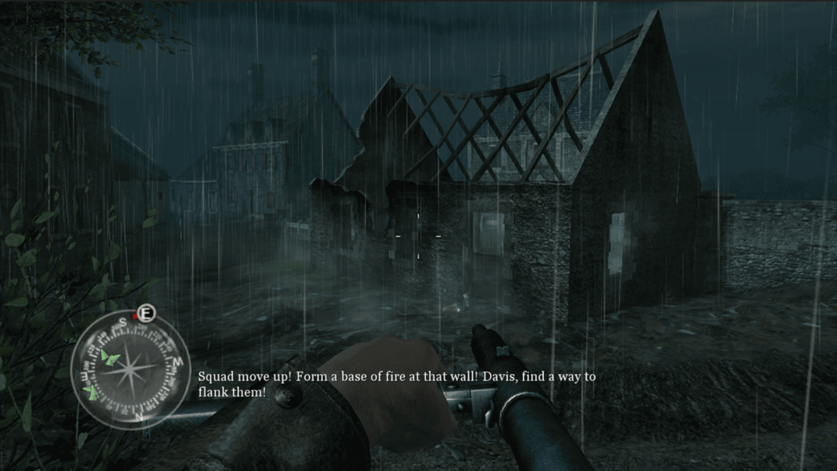 An in-game screenshot of Call of Duty 2, showcasing the player character advancing on a bombed house in heavy rain, armed with a Sten machine gun.