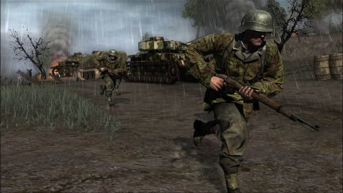 An in-engine screenshot of Call of Duty 3, showcasing two soldiers running in the rain, against the backdrop of bombed-out tanks.
