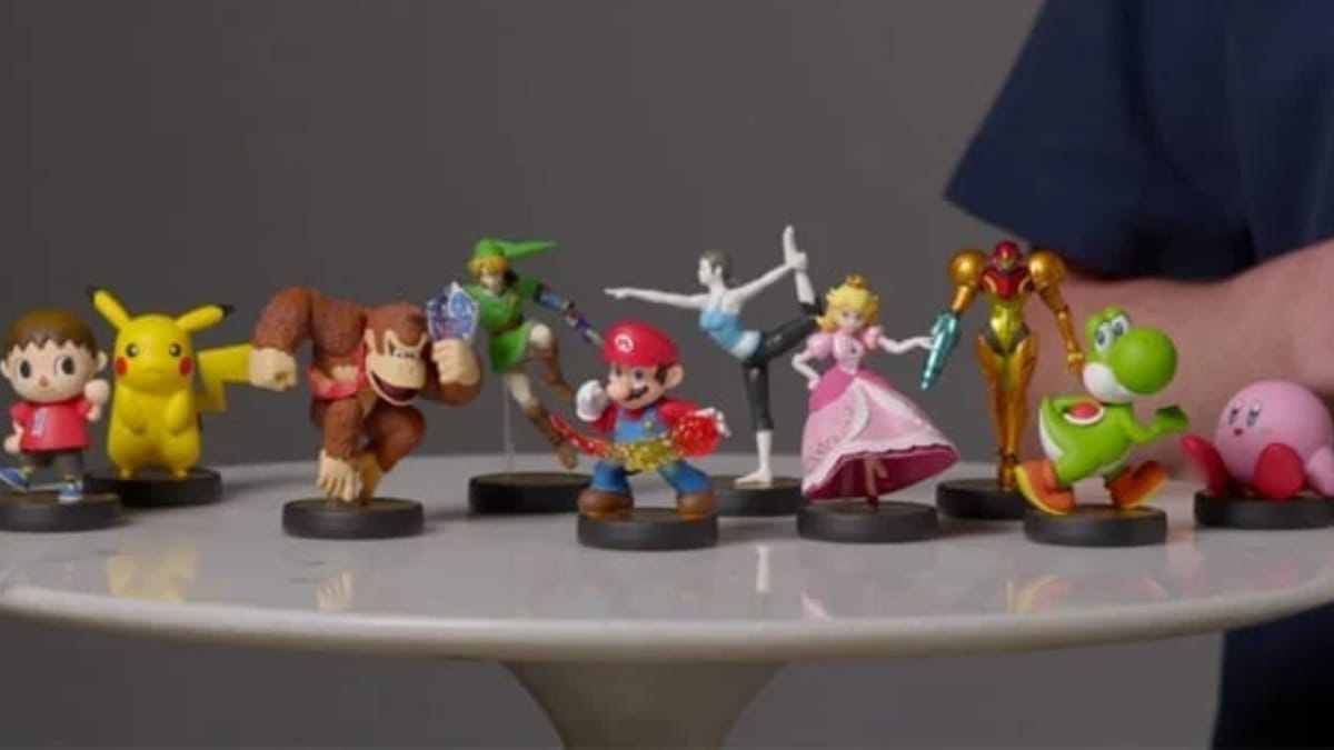 Nintendo E3 2014 photo showing various Amiibo figures of Nintendo characters sat on a table with a man in a blue button up shirt sat behind them.