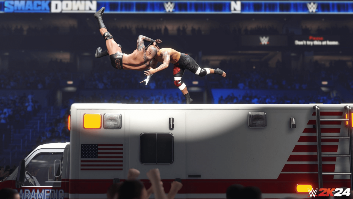 An in-engine screenshot of WWE 2k24, showcasing two wrestlers battling each other on top of an ambulance within the ring.