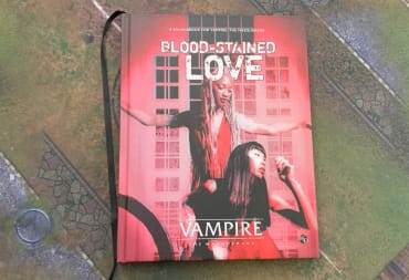 A hardcover copy of Vampire: The Masquerade Blood-Stained Love sitting on a gaming mat.