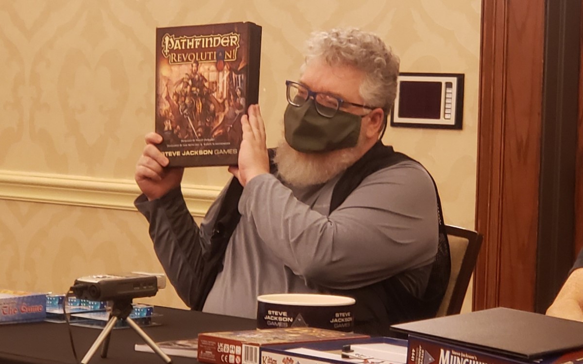 A panelist holding up a mock up box of Pathfinder Revolution