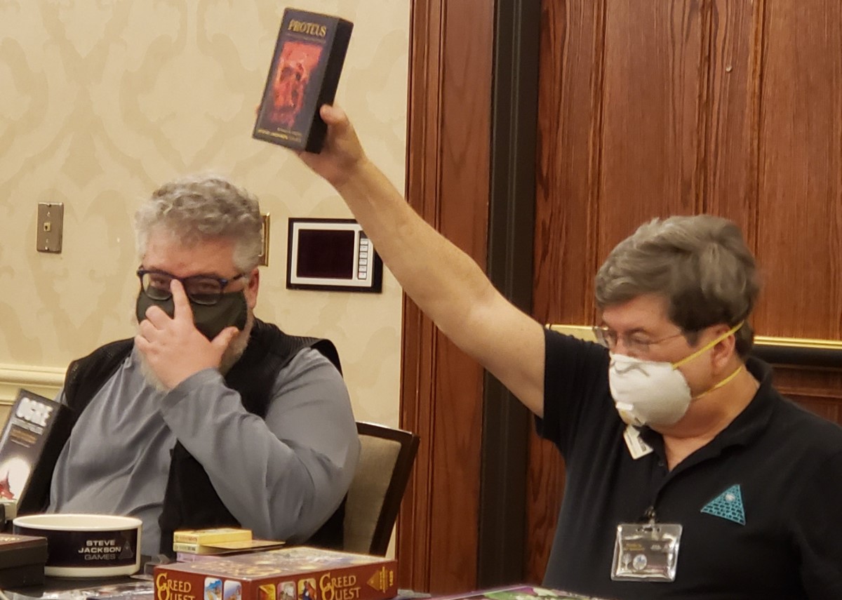 Panelists holding up a pocket box of Proteus at a Fnordcon 2022 panel