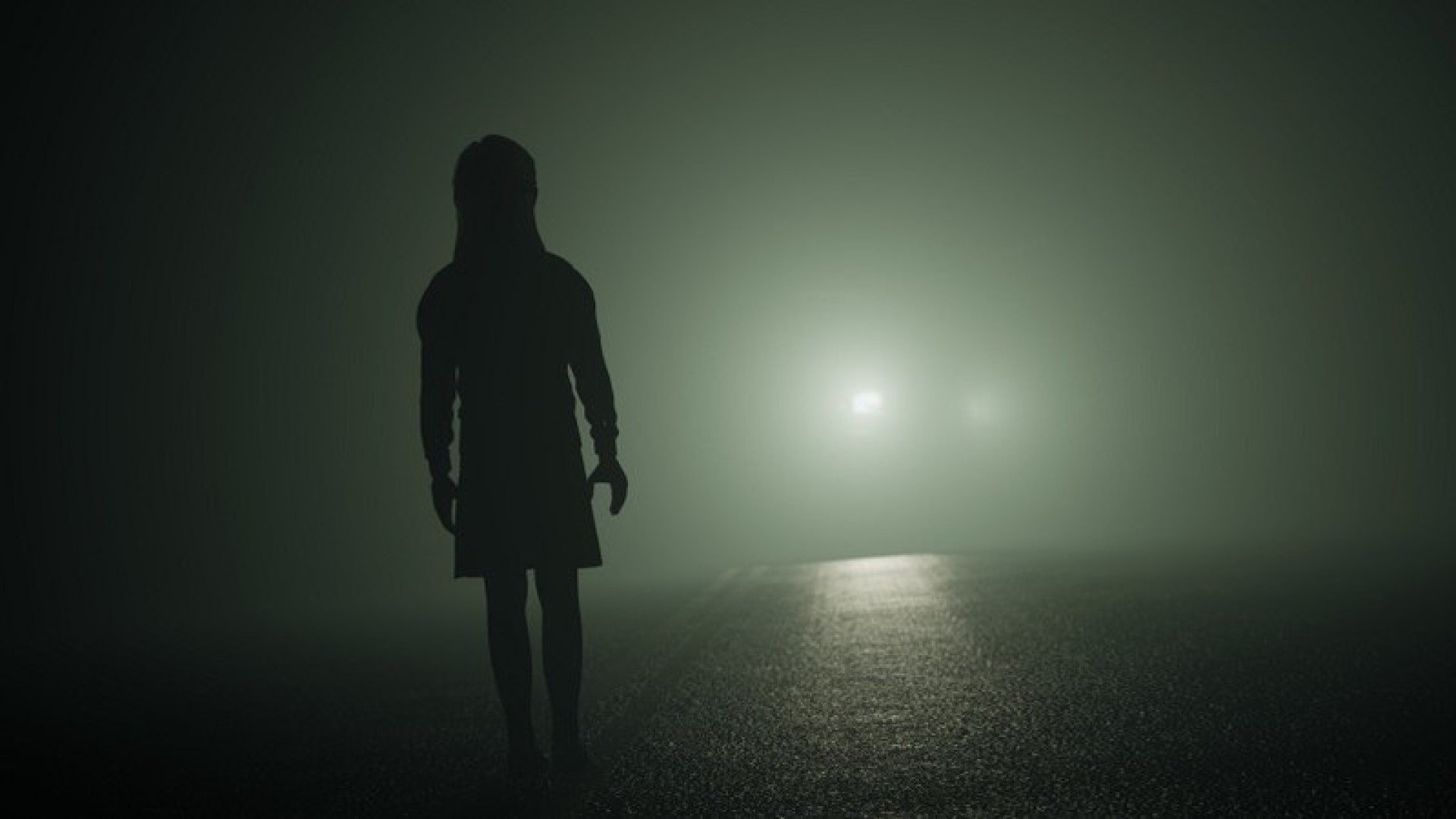 A creepy little girl in silhouette of a flashlight through the fog