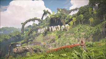 Aloy looking at a ruined Hollywood sign, the body of a large robot sitting in the background from Horizon Forbidden West: Burning Shores