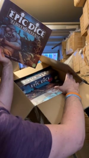 A member of Golden Bell Games in a Garage Holding a copy of Epic Dice