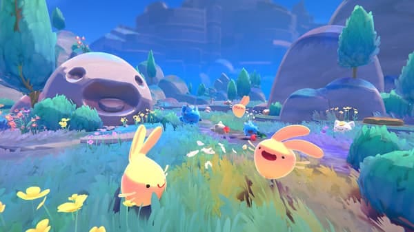Slime Rancher 2 screenshot in game of the slimes bouncing around the grasslands with rock statues in the background with slime faces carved into them, smiling and just looking as cute as ever 