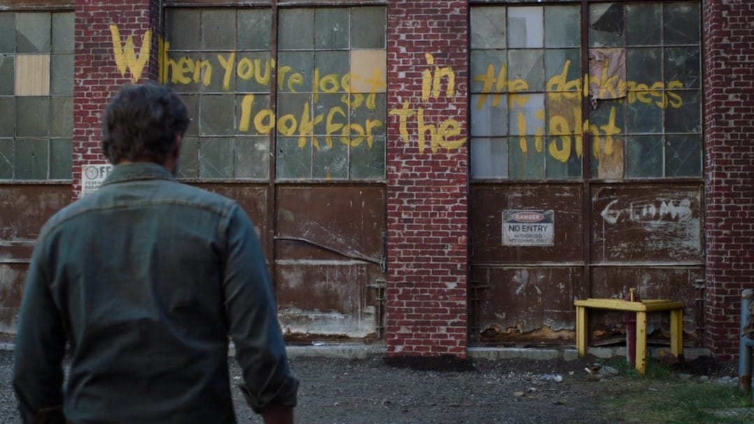 A screenshot from HBO's The Last of Us of a message on a brick wall stating, "When You're Lost in the Darkness, Look For The Light."