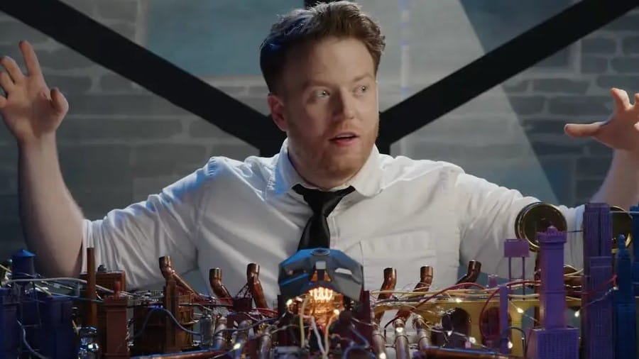 A set photo of the Dimension 20 campaign Mentopolis, featuring Brennan Lee Mulligan in front of an elaborate miniature city model