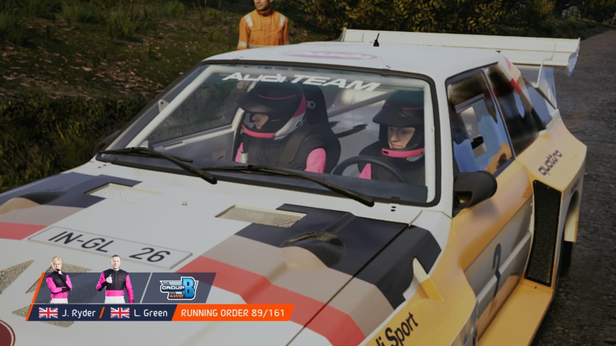 EA Sports WRC screenshot showing two drivers in pink team uniforms sitting in a rally car waiting for a race to start 