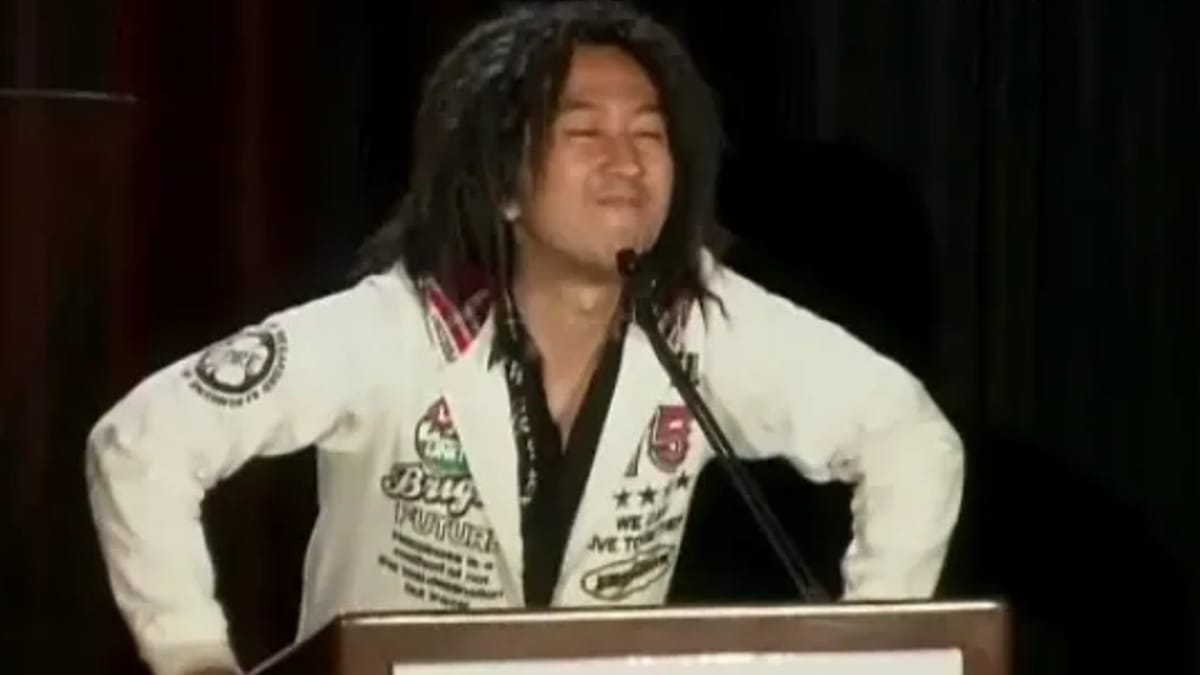 Tak Fujii can be seen standing on a podium, grinning.