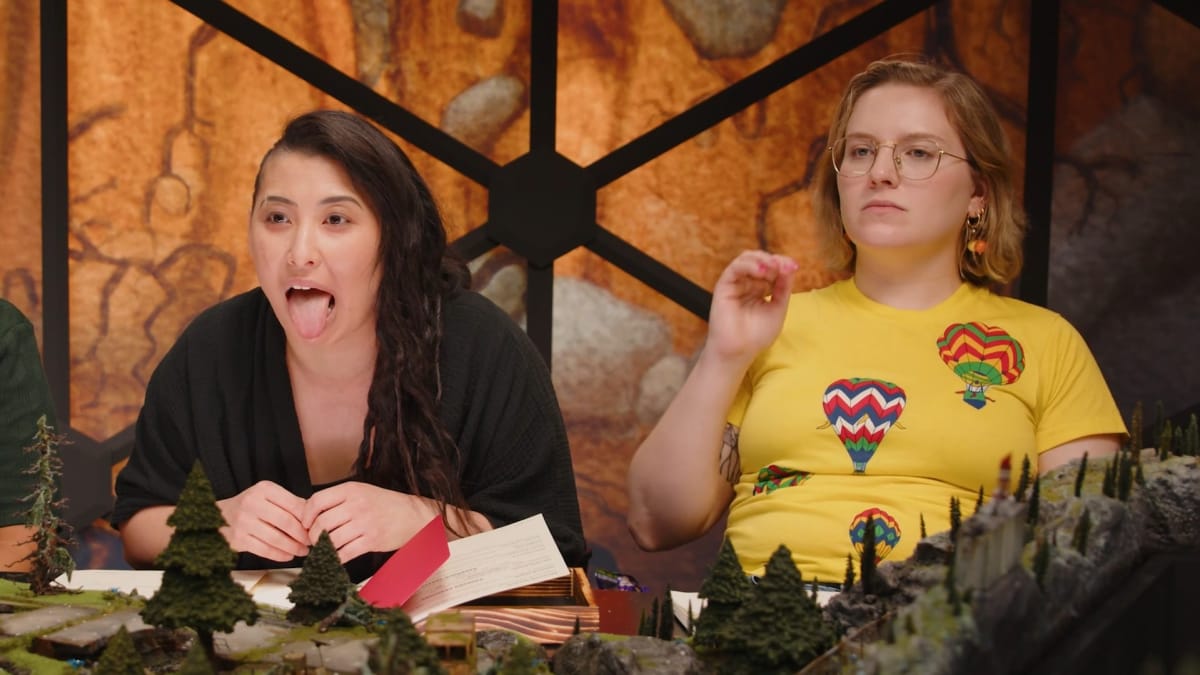 Erika scaring Izzy at the table performing as Ava in Dimension 20: Burrow's End