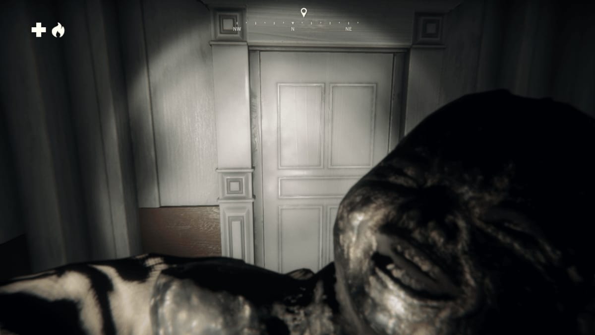 An in-game screenshot of Kona II: Brume, showcasing the player walking through a dark hallway, with a flashlight illuminating a door, as well as a bust of a laughing baby.