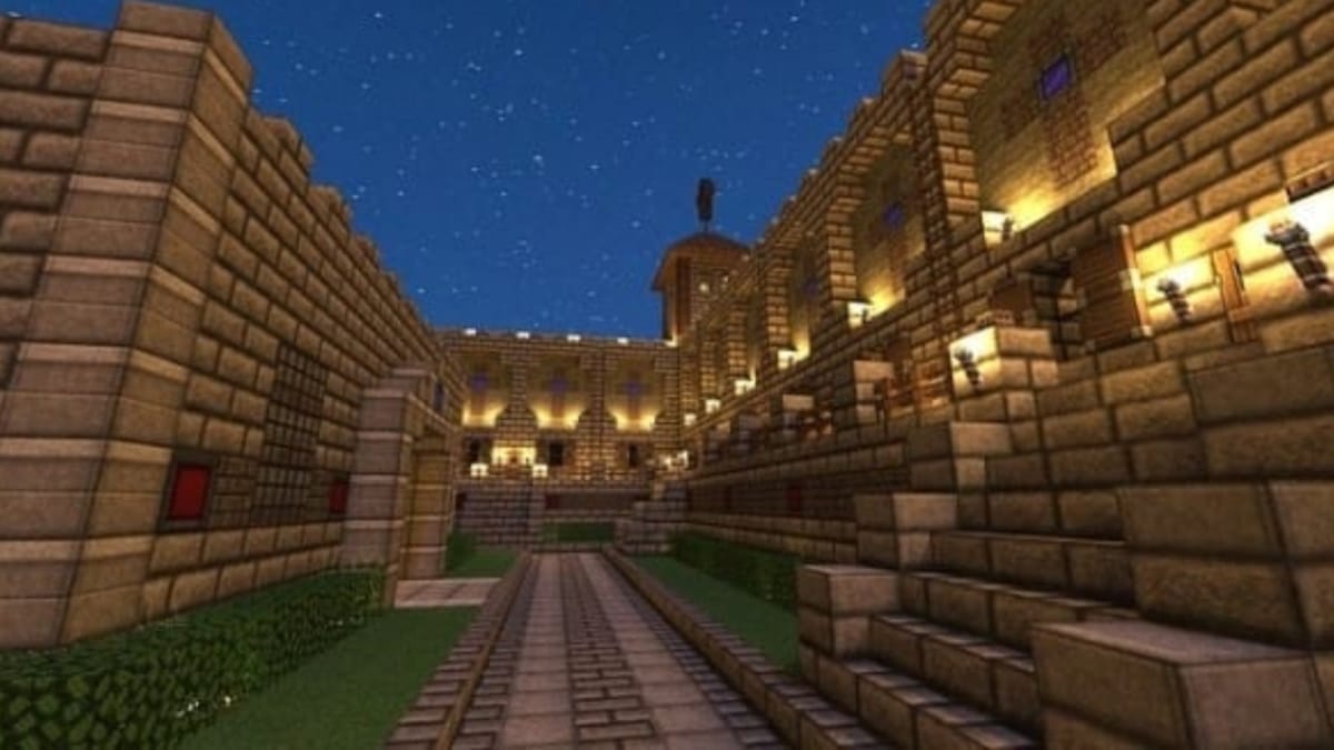 Minecraft screenshot showing a complex structure built out of brick with highly decorated gravel paths lined with grass and lowers. 