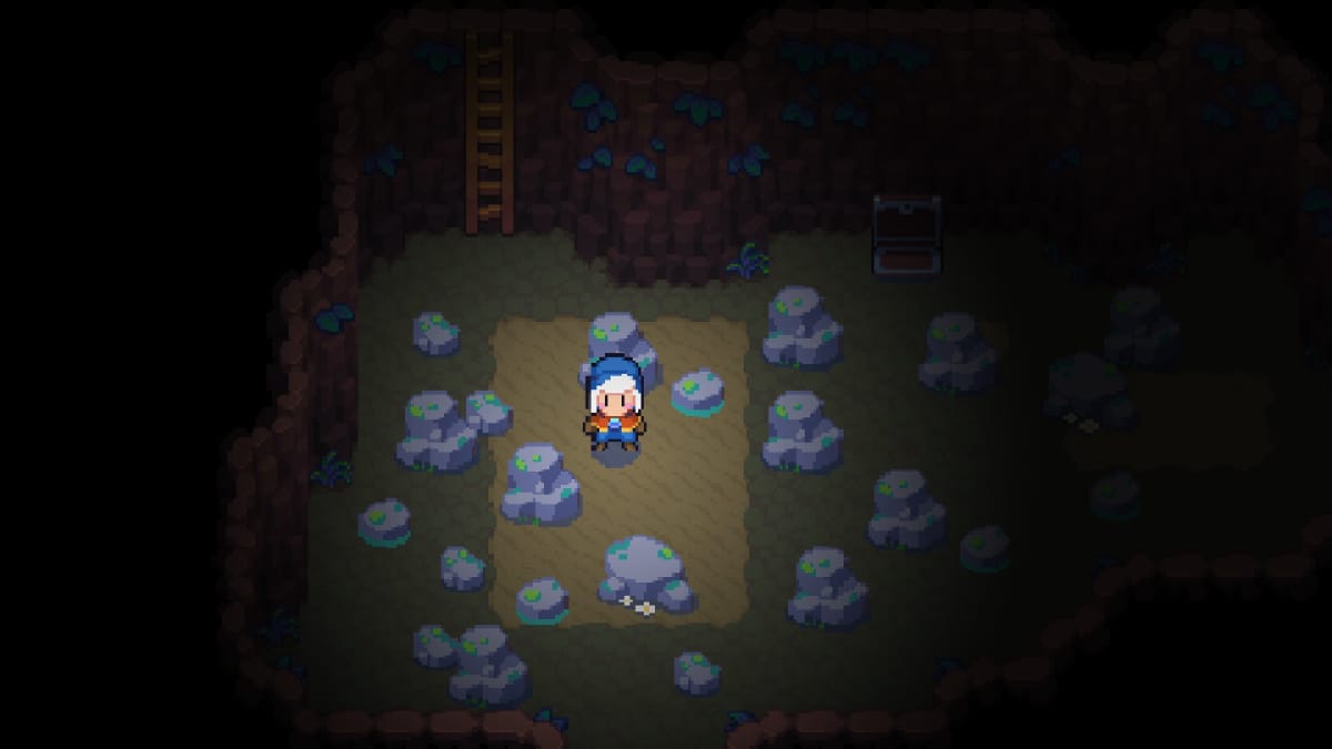 Moonstone Island screenshot showing a pixel art character in a blue hat standing in a dark mine shaft surrounded by boulders