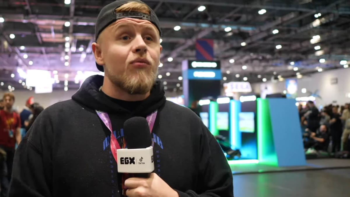 A presenter talking into a microphone branded with the logo for the ReedPop event EGX