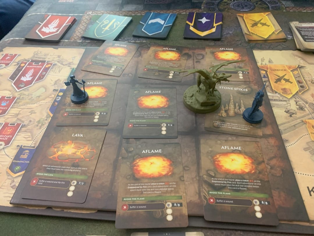 A screenshot from Runescape Kingdoms Shadow of Elvarg showing a grid covered in cards with flames on them, two miniatures of adventurers, and a dragon miniature.
