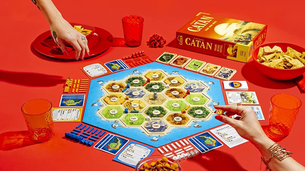 The board game Catan set on a red background with 1950s illustrated hands interacting with the pieces
