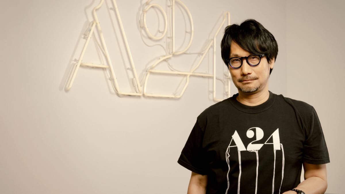Hideo Kojima standing in front of an A24 logo and wearing an A24 shirt for the Death Stranding movie