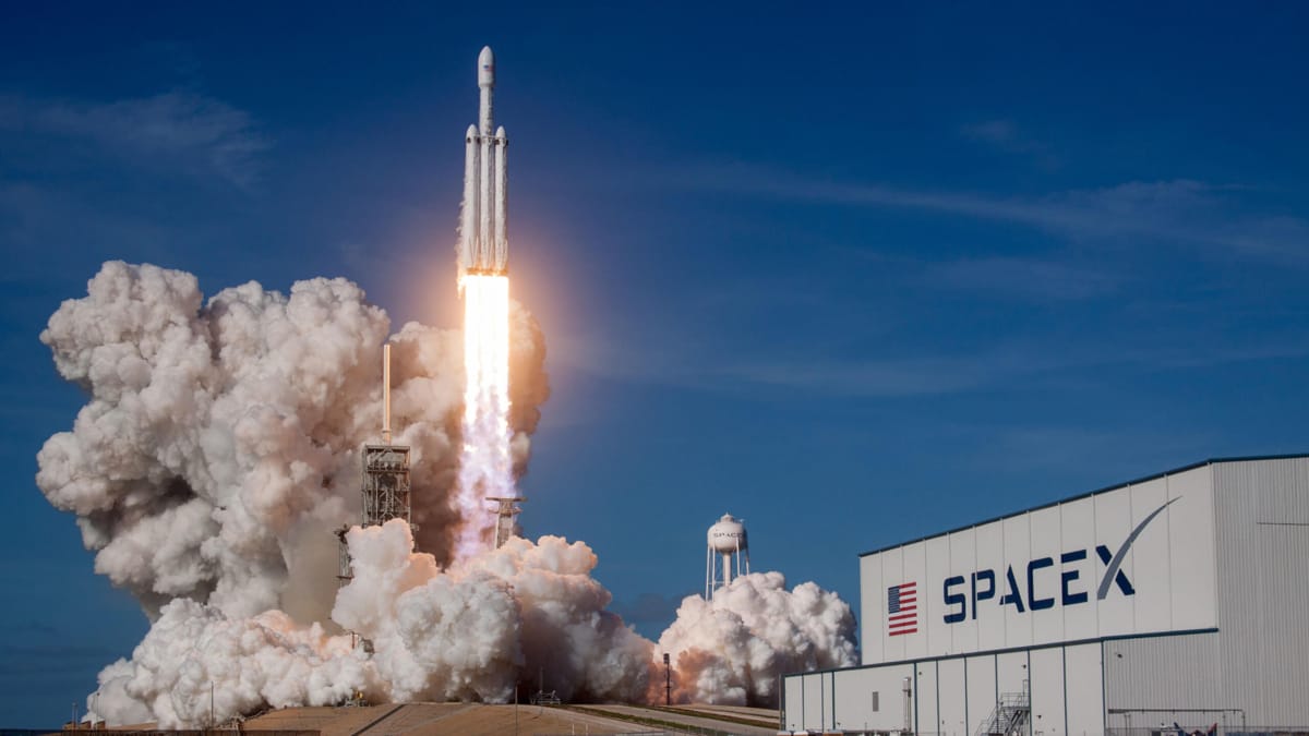 A rocket launching next to a building with the SpaceX logo