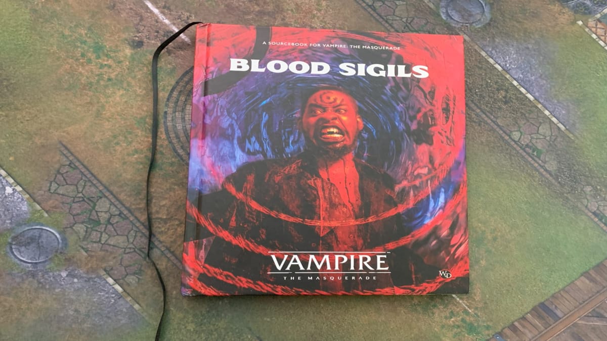 A hardcover copy of Vampire: The Masquerade Blood Sigils sitting on a gaming mat.