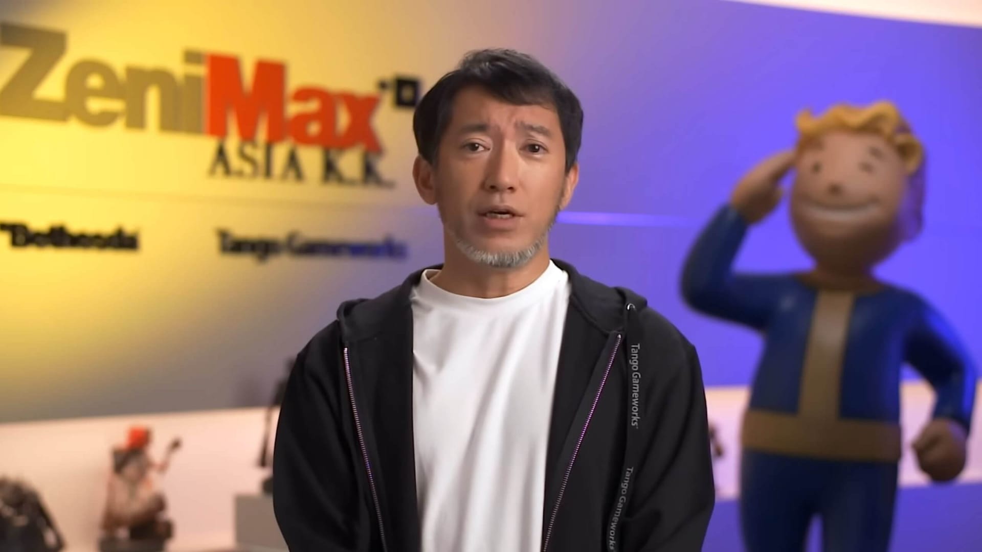 Shinji Mikami speaking in front of a ZeniMax background