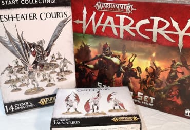 photo showing several boxes for the game WarCry with various miniatures sat on the table in front of the boxes. 
