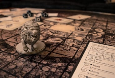 Kingdom Death Monster Board With Lion Figurine in the foreground and a character sheet in the bottom right. 