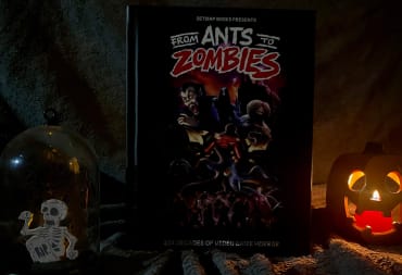 A picture showcasing the front cover of From Ants to Zombies, with a glowing ceramic pumpkin and skeleton diorama sitting on each side, against a soft grey backdrop.