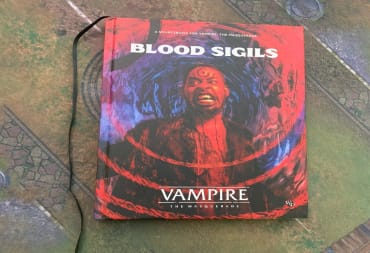 A hardcover copy of Vampire: The Masquerade Blood Sigils sitting on a gaming mat.